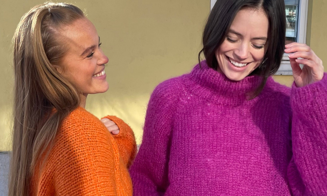 Two Scandinavian girls wearing chunky oversized sweaters in orange and purple yarn