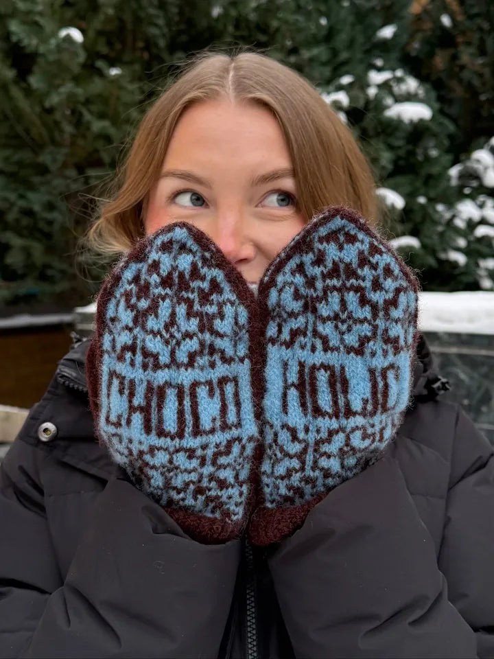 A knitter holding up finished colorwork mittens in blue and brown